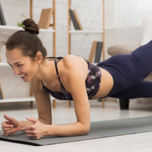 Fit woman doing yoga plank and watching online tutorials on laptop, training in living room